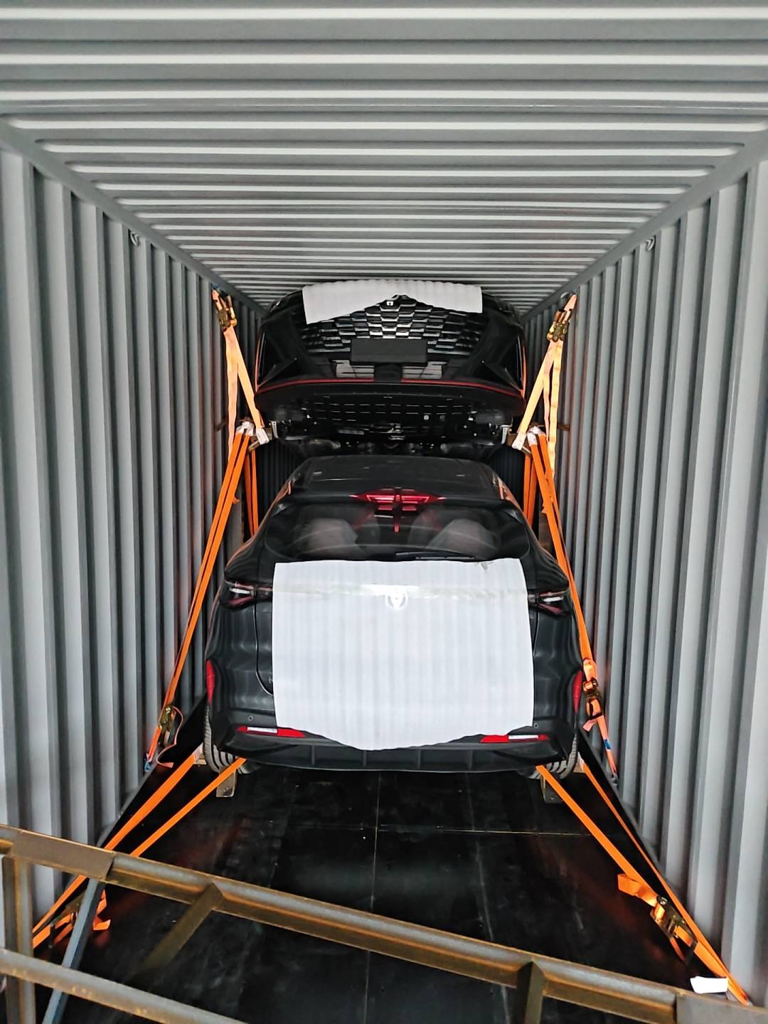 Vehicles in a container with protective coverings and orange securing straps